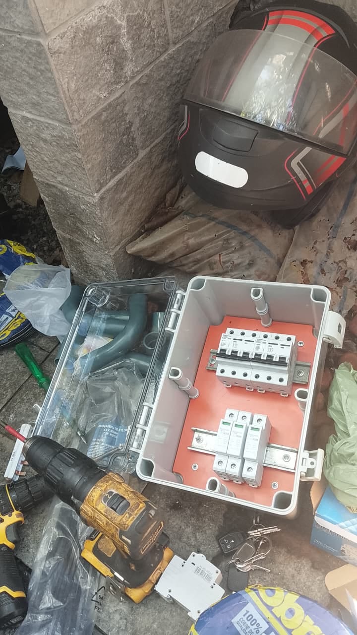 Quadro de distribuição elétrico aberto com disjuntores instalado numa parede de tijolinho, com capacete de mot
