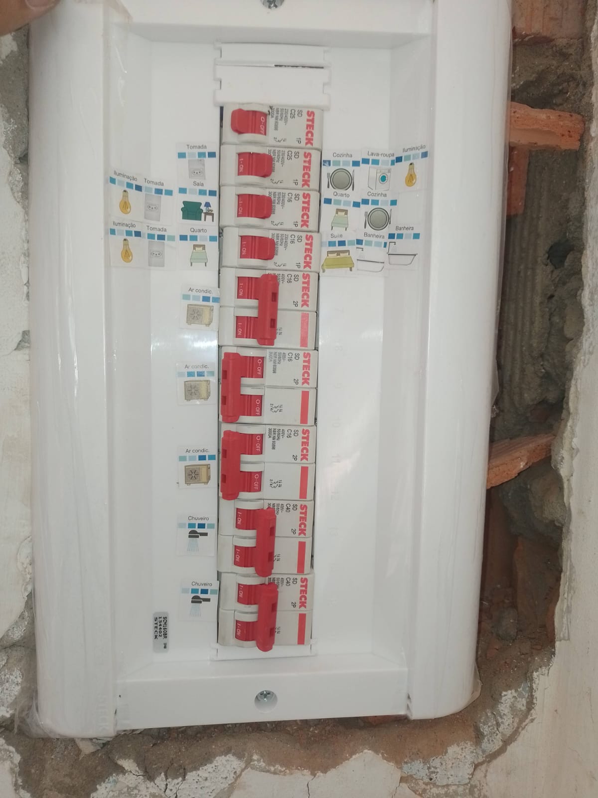 Quadro de distribuição elétrico branco com disjuntores vermelhos da marca Steck, com etiquetas adesivas…